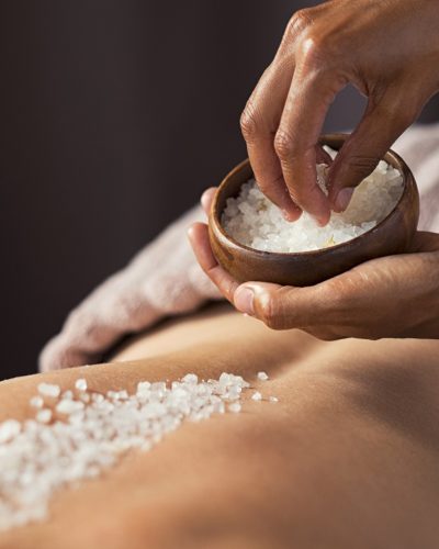 Masseuse hands doing massage on woman's back at beauty salon. Beauty therapist pouring salt scrub on woman back at health spa. Scrubbing and skin care concept.