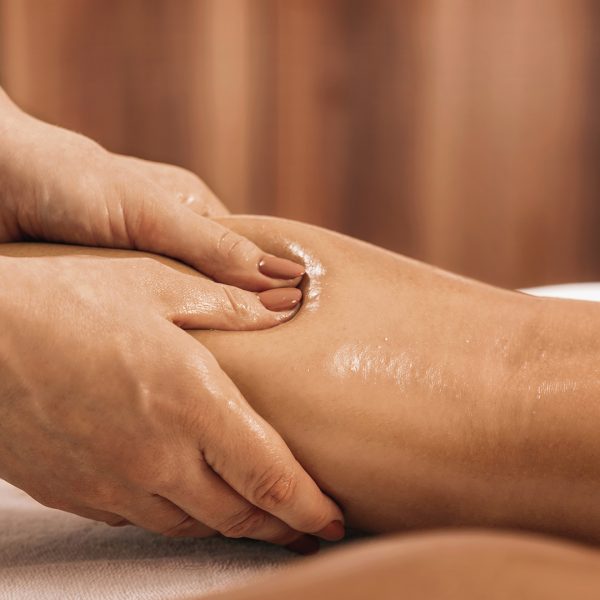 Lymphatic drainage massage. Hands of a masseuse massaging leg of a female client