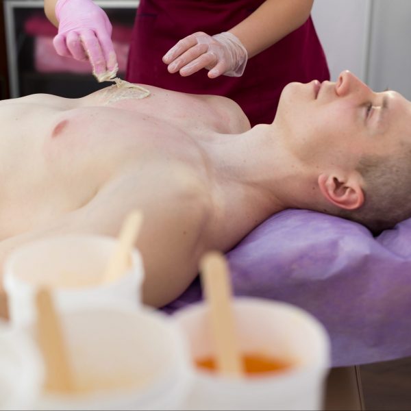 Woman beautician puts a thick sugar paste on the mans chest making him hair removal. A young guy with inflated muscles removes hair from his chest in a beauty salon. Shugaring